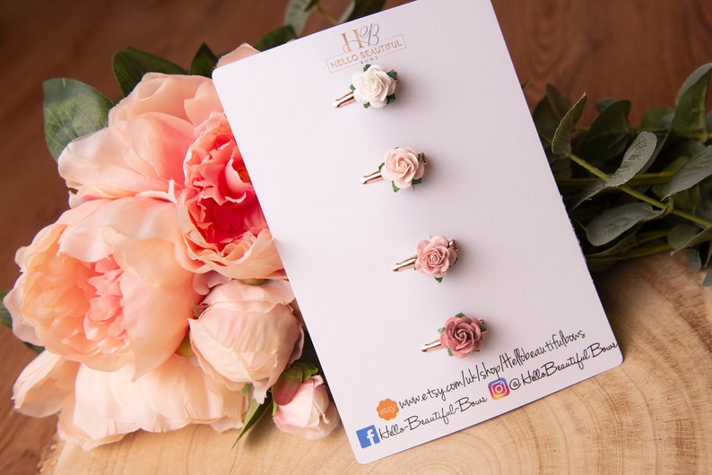 May include: Four pink and white flower hair clips on a white card with the text "Hello Beautiful Bows" and website information.