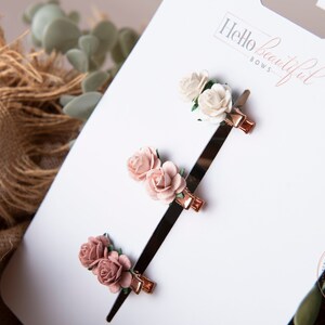 May include: Three sets of rose hair clips on a white card with the text "Hello beautiful bows". The clips are in shades of pink and white.