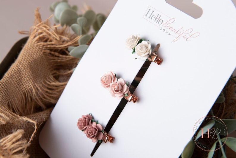 May include: Three sets of rose hair clips on a white card with the text "Hello beautiful bows". The clips are in shades of pink and white.