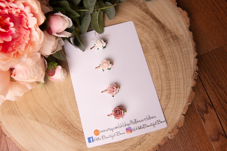 May include: Three pink and white flower hair clips on a white card with the text "Hello Beautiful Bows" and social media handles.