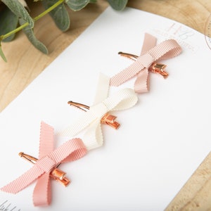 May include: Three hair clips with pink and white satin bows. The bows are tied in a simple knot and the clips are gold.