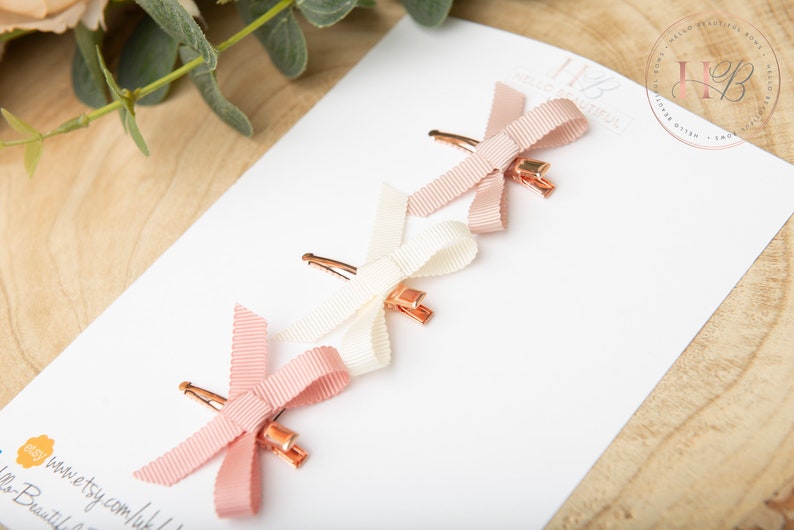 May include: Three hair clips with pink and white satin bows. The bows are tied in a simple knot and the clips are gold.