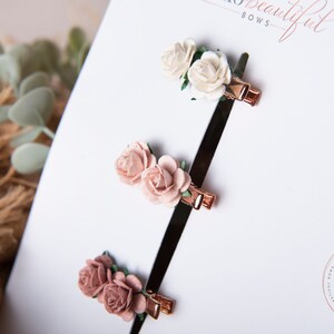 May include: Three sets of hair clips, each featuring two small fabric roses. The roses are in shades of pink and white. The clips are gold coloured.