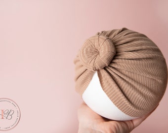 May include: A brown ribbed turban with a knotted top. The turban is made of a soft, stretchy fabric and is perfect for adding a touch of style to any outfit.