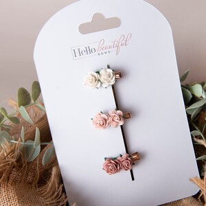 May include: Set of three floral hair clips with two pink and one white flower. The clips are on a white card with the text "Hello beautiful bows".