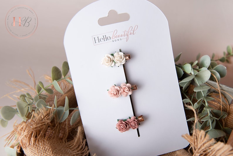 May include: Set of three floral hair clips with two pink and one white flower. The clips are on a white card with the text "Hello beautiful bows".