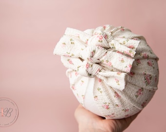 May include: A white and pink floral fabric headband with a knotted bow. The headband is made of a soft, stretchy fabric and is perfect for newborns and babies.