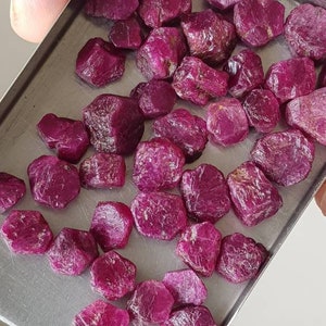 Può includere: Una collezione di pietre preziose di rubino in un vassoio di metallo. I rubini sono di varie tonalità di rosa e rosso.