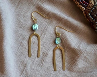 Könnte beinhalten: Ein Paar goldene Ohrringe mit einer einzigartigen Bogenform und einem blauen, schillernden Edelstein-Akzent.