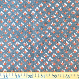 May include: Close-up of a fabric with a repeating pattern of white and orange geometric shapes on a teal background. A wooden ruler with inch markings is at the bottom of the image.