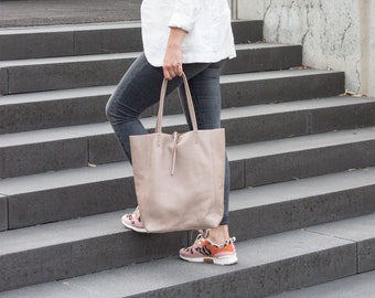 Könnte beinhalten: Eine Frau in einem weißen Blazer, grauen Jeans und rosa-orangenen Sneakern trägt eine hellbraune Tote Bag, während sie eine Betontreppe hinunterläuft.