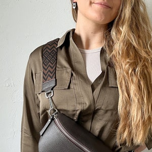 May include: A brown leather crossbody bag with a zipper closure and a patterned strap. The strap is brown, black, and orange with a geometric design.