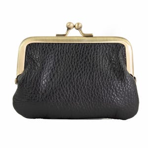 May include: A black leather coin purse with a textured surface. The purse has a brass-colored metal frame and clasp closure. The coin purse is a small, compact accessory.