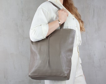 Könnte beinhalten: Eine taupefarbene Ledertasche mit minimalistischem Design. Die Tasche hat eine rechteckige Form mit einem langen, dünnen Riemen und einer strukturierten Oberfläche. Die Tasche wird von einer Person getragen, die ein weißes Hemd und eine Hose trägt.