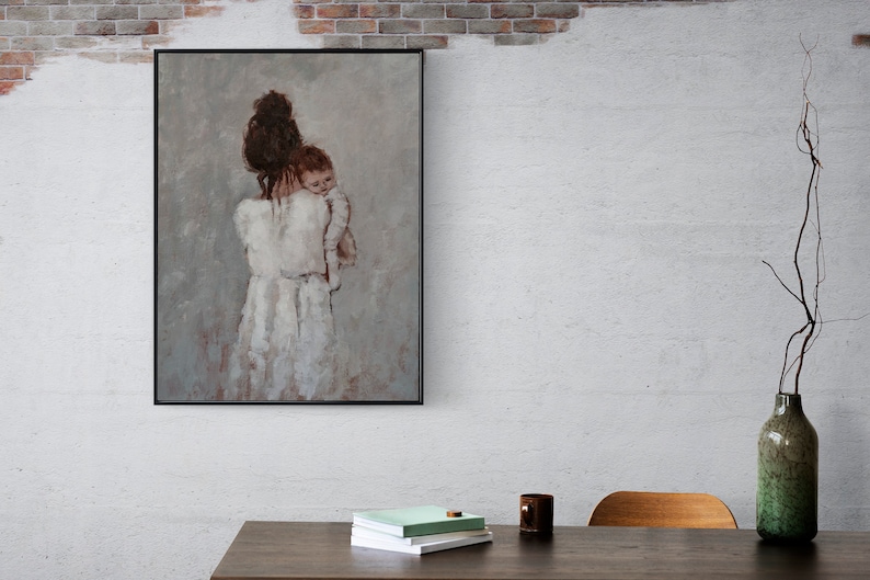 May include: A framed painting of a woman holding a child in her arms. The woman is wearing a white dress and the child is wearing a white onesie. The painting is set against a light gray background.