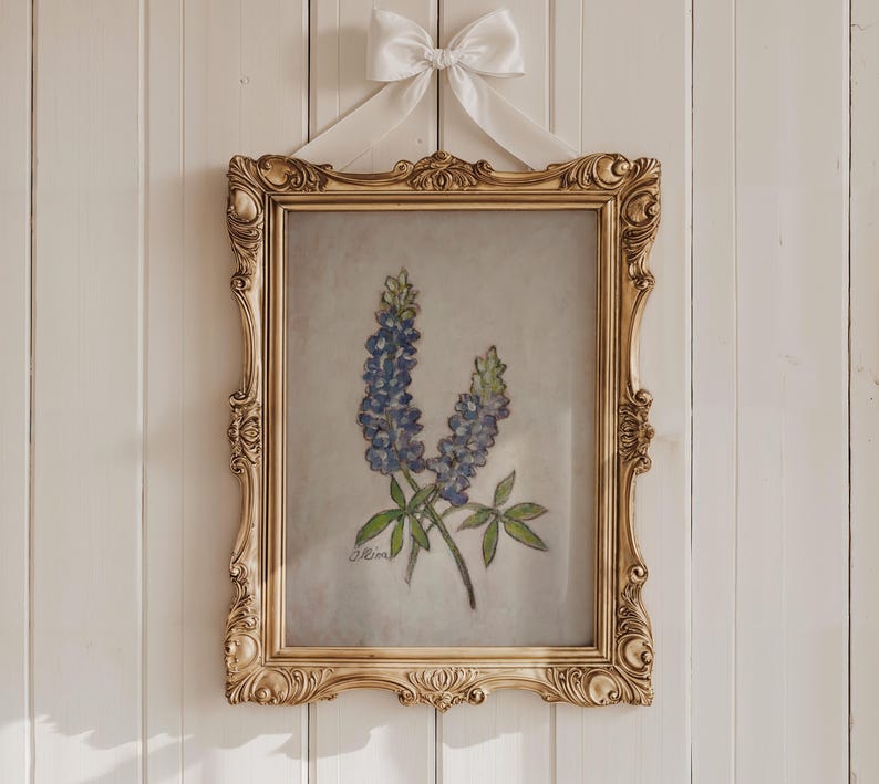 May include: A framed painting of bluebonnet flowers in a gold ornate frame. The painting is on a white background and the frame is hanging on a white wall.