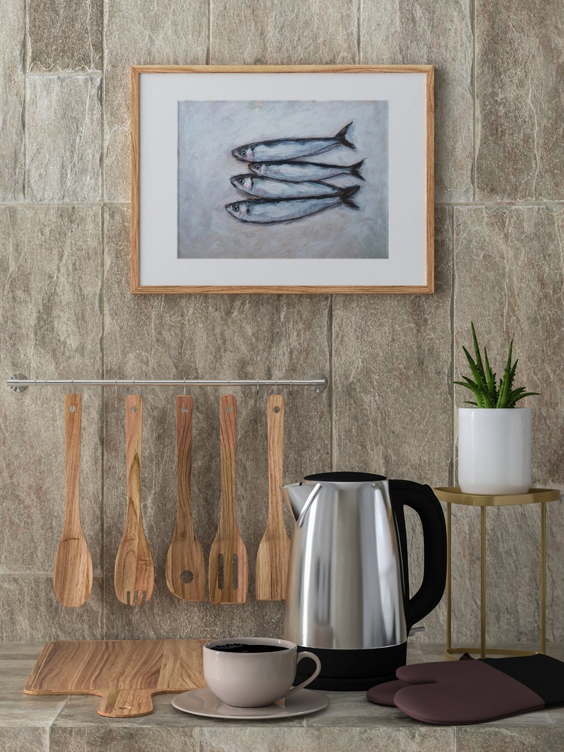 K&ouml;nnte beinhalten: Eine K&uuml;chenarbeitsplatte mit einem elektrischen Wasserkocher aus Edelstahl, einem Schneidebrett aus Holz, einem Satz Holzl&ouml;ffel, einer wei&szlig;en Tasse mit Kaffee und einem gerahmten Bild von f&uuml;nf silbernen Fischen.