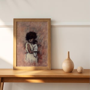 May include: A framed art print shows a mother and baby in soft pink, white, and brown tones. The artwork is in a light brown wooden frame. A wooden vase and sphere are on a wooden table. The image evokes a sense of tenderness.