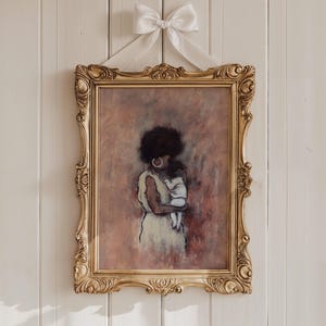May include: An artwork in a gold ornate frame, showing a mother and child. The painting uses soft pastel colours. A white bow is at the top. The mother has dark hair and wears a light dress. The frame is hung on a white wall.