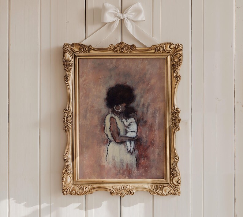 May include: An artwork in a gold ornate frame, showing a mother and child. The painting uses soft pastel colours. A white bow is at the top. The mother has dark hair and wears a light dress. The frame is hung on a white wall.
