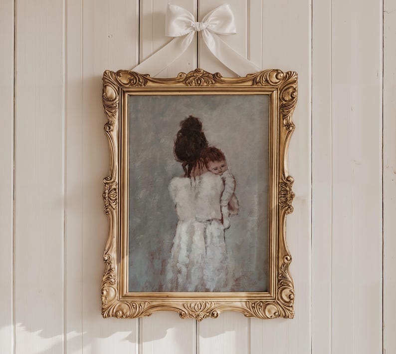 May include: A gold framed painting of a woman holding a baby in her arms. The woman and baby are both wearing white clothing. The painting has a soft, muted color palette.