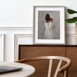 May include: A framed painting of a woman in a white dress holding a baby. The painting is on a wooden shelf with a potted plant and a laptop on a table in the foreground.