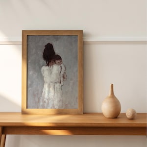Könnte beinhalten: Ein gerahmtes Kunstwerk zeigt eine Mutter, die ein Baby hält, in sanften, gedämpften Tönen. Das Gemälde zeigt eine Frau in einem weißen Kleid und ein Kind vor grauem Hintergrund. Das Kunstwerk befindet sich in einem hellbraunen Holzrahmen.