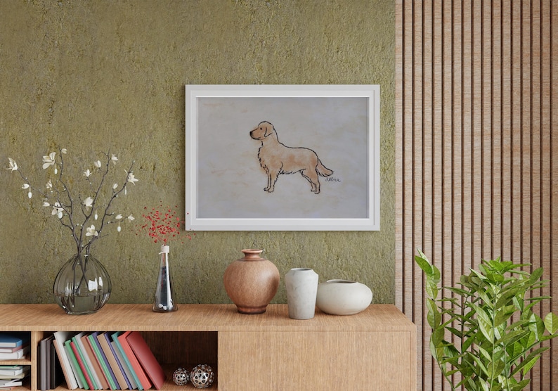 May include: A framed artwork featuring a golden retriever dog illustration. The dog is depicted in profile, with a light brown coat and a black outline. The artwork is displayed on a wall above a wooden cabinet with decorative vases and books.