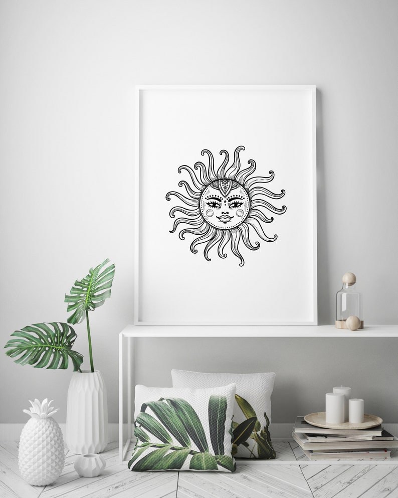 May include: A black and white illustration of a sun with a face and intricate details. The sun is framed in a white frame and is hanging on a white wall. The wall is decorated with a white vase with a green plant, a white pineapple, and a white shelf with a glass bottle, a wooden knob, and two white candles.