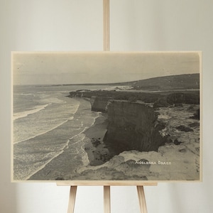 Puede incluir: Una postal vintage en blanco y negro con una vista panorámica de una costa rocosa con olas rompiendo. El texto "Anglesea Beach" está impreso en la parte inferior de la postal.