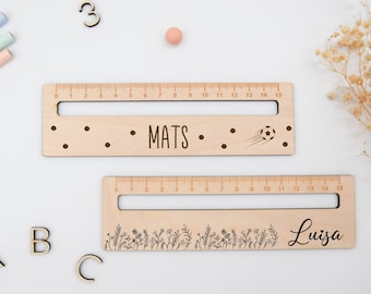 Puede incluir: Dos reglas de madera con nombres personalizados, "Mats" y "Luisa". La regla con "Mats" tiene un diseño de balón de fútbol, mientras que la regla con "Luisa" tiene un diseño floral.