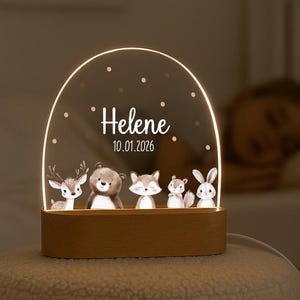 Könnte beinhalten: Ein bogenförmiges Acryl-Nachtlicht mit Holzsockel, bedruckt mit Illustrationen von Reh, Bär, Fuchs, Eichhörnchen und Hase. Der Text "Helene" und "10.01.2026" ist in Weiß mit kleinen Punkten aufgedruckt und strahlt ein warmes Licht aus.