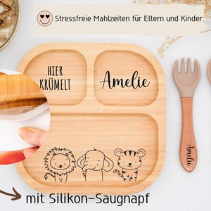 K&ouml;nnte beinhalten: Ein geteilter Holzteller mit dem Namen "Amelie" und dem Schriftzug "Hier Kr&uuml;melt". Der Teller zeigt Illustrationen eines L&ouml;wen, eines Elefanten und eines Tigers. Eine Gabel und ein L&ouml;ffel mit Holzgriffen sind ebenfalls enthalten.
