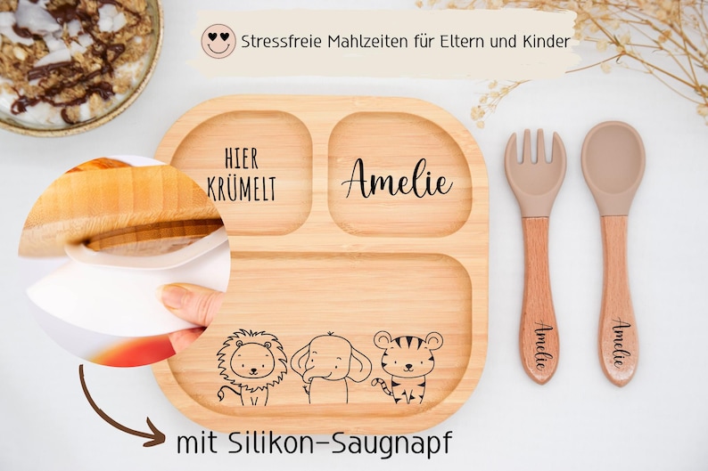 K&ouml;nnte beinhalten: Ein geteilter Holzteller mit dem Namen "Amelie" und dem Schriftzug "Hier Kr&uuml;melt". Der Teller zeigt Illustrationen eines L&ouml;wen, eines Elefanten und eines Tigers. Eine Gabel und ein L&ouml;ffel mit Holzgriffen sind ebenfalls enthalten.