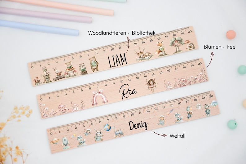May include: Three light-coloured wooden rulers, each 20 cm long, featuring printed illustrations and names. The top ruler shows woodland animals and the name LIAM. The middle ruler displays floral fairy motifs and the name Ria. The bottom ruler features space-themed graphics and the name Deniz.