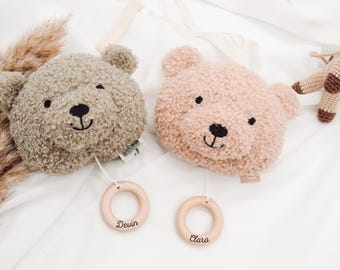 May include: Two plush bear head baby mobiles in taupe and blush pink, with embroidered black eyes and smiles. Each has a wooden ring with a name, and a crocheted horse toy. A soft, neutral-toned nursery decor.