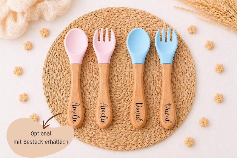 K&ouml;nnte beinhalten: Vier Baby-Essbestecke: zwei L&ouml;ffel und zwei Gabeln. Die L&ouml;ffel- und Gabelk&ouml;pfe sind rosa und blau, mit Holzgriffen. Die Griffe sind mit Namen graviert. Das Besteck ist auf einer gewebten Matte angeordnet.