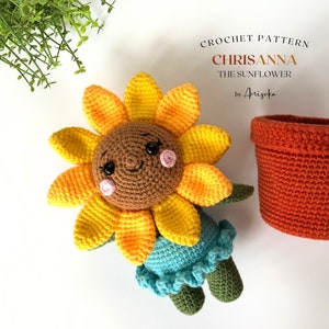 May include: Crochet pattern for a sunflower amigurumi toy called Chrisanna. The sunflower is yellow and orange with a brown face and pink cheeks. The sunflower is sitting in a brown crochet pot. The pattern is by Arisuka.