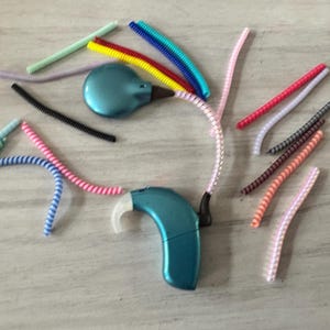 May include: A teal blue hearing aid with a variety of colorful coiled cords. The cords are in various colors, including pink, blue, green, red, and yellow.