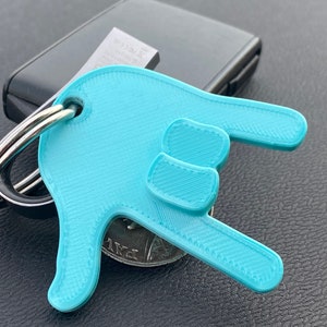 May include: A light blue plastic keychain shaped like a hand making the 'rock on' hand gesture. The keychain is attached to a silver key ring.