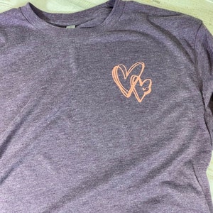 May include: A purple heather long-sleeved t-shirt with a pink graphic of two intertwined hearts.