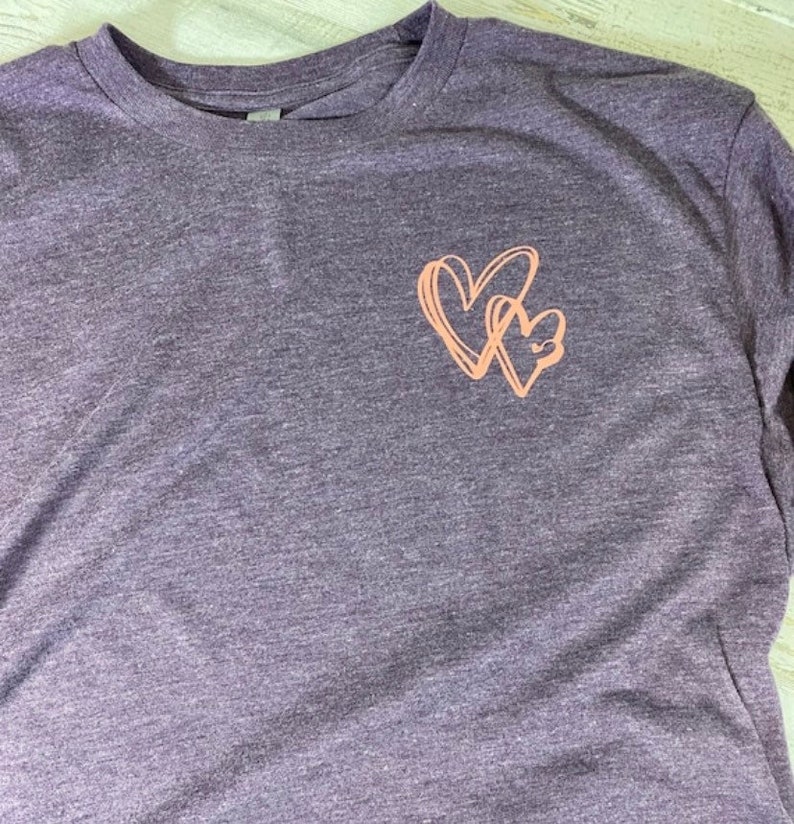 May include: A purple heather long-sleeved t-shirt with a pink graphic of two intertwined hearts.