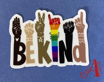 May include: A sticker with the word "BE KIND" in black, brown, and beige letters. The letters are formed by hands in different skin tones signing the word in American Sign Language. The hands are decorated with hearts, stars, and rainbow bracelets.
