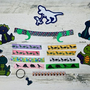 以下が含まれることがあります： カラフルな布のリボン、アイロン接着パッチ、キーホルダーなど、恐竜をテーマにしたクラフト用品のコレクション。パッチには、トリケラトプス、ステゴサウルス、ティラノサウルス・レックスなど、さまざまな恐竜が描かれています。