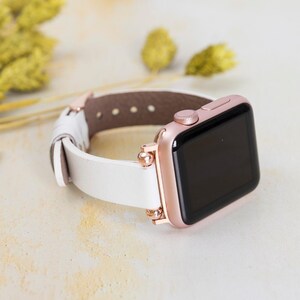 May include: Rose gold smartwatch with a white leather strap. The watch face is black, and the strap is secured with rose gold hardware. A modern accessory suitable for everyday wear.