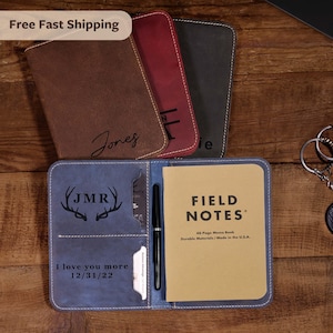 May include: A collection of leather notebooks in various colors, including brown, red, and blue. The blue notebook is open, revealing a Field Notes memo book and a pen. The notebooks are personalized with names and initials.