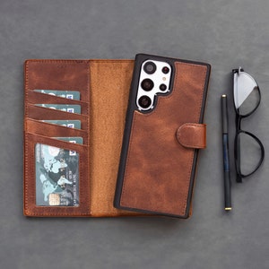 May include: A brown leather wallet and phone case set with a black border. The wallet is open, revealing card slots with credit cards. A black pen and glasses are next to the phone case.