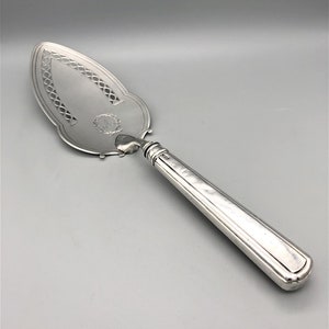 May include: A silver cake server with an ornate handle and a decorative, pierced blade. The blade has a monogram in the center.