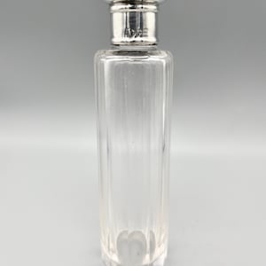 May include: A clear glass bottle with a silver stopper. The bottle has a textured, ribbed design and a rounded bottom.