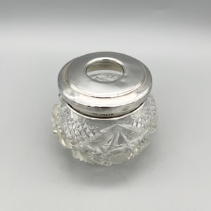 Könnte beinhalten: Eine klare Glasdose mit geschnittenem Glasdesign und einem silbernen Deckel. Der Deckel hat eine kreisförmige Öffnung in der Mitte.
